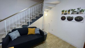 Ein Wohnzimmer mit schwarzem Sofa, einer Treppe und Wandkunst mit Pflanzen.