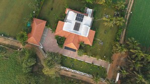 An aerial view of a house with a solar panel roof, surrounded by lush greenery and palm trees. - PRABANCH GARDENS - A CONSCIOUS STAY (Chengalpattu)