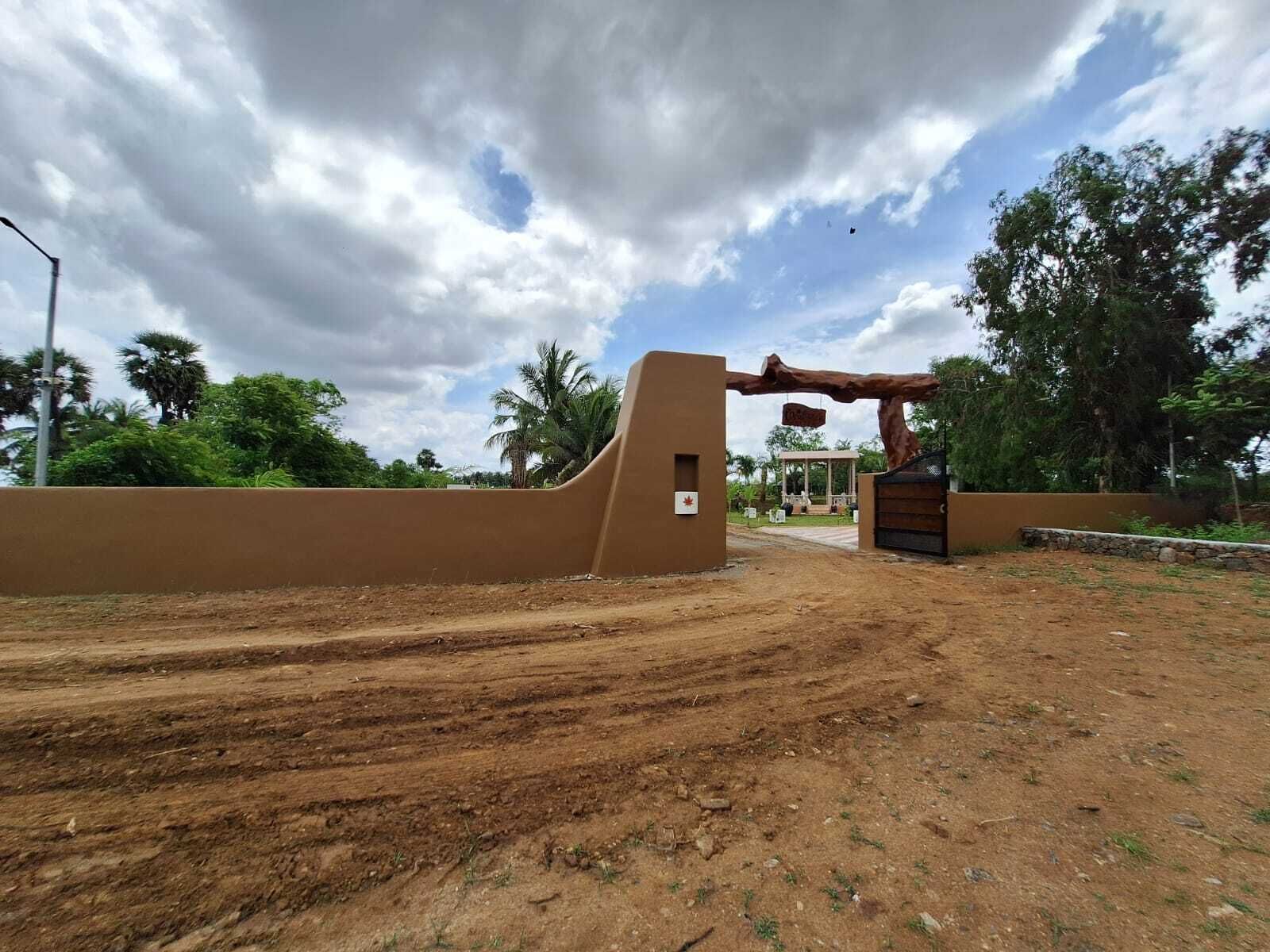 A dirt road leading to a gated entrance with a wooden archway and a small signboard.