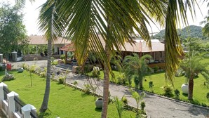 A well-maintained garden with palm trees, a paved walkway, and a building with a tiled roof. - PRABANCH GARDENS - A CONSCIOUS STAY (Chengalpattu)