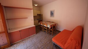 A compact room with a dining table, a sofa, and a kitchenette. - Apartment Retreat near the Adriatic Sea (Rosolina Mare RO)