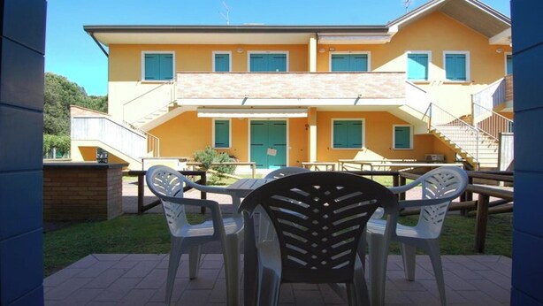 A two-story building with a yellow facade, a green door, and multiple windows. There is a patio area with outdoor furniture. - Apartment in Rosolina for six guests (Rosolina Mare RO)