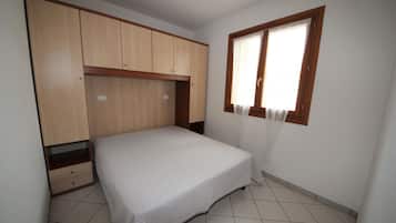 Een slaapkamer met een bed, een houten garderobe en een raam met gordijnen.