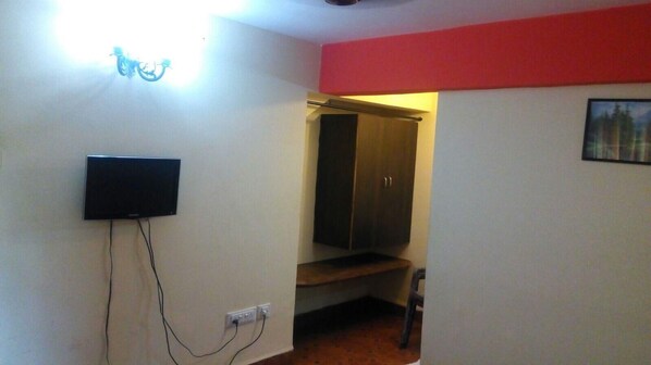A room with a television mounted on the wall, a wardrobe, and a small bench. - Ginger Tree Boutique Resort (Anjuna)