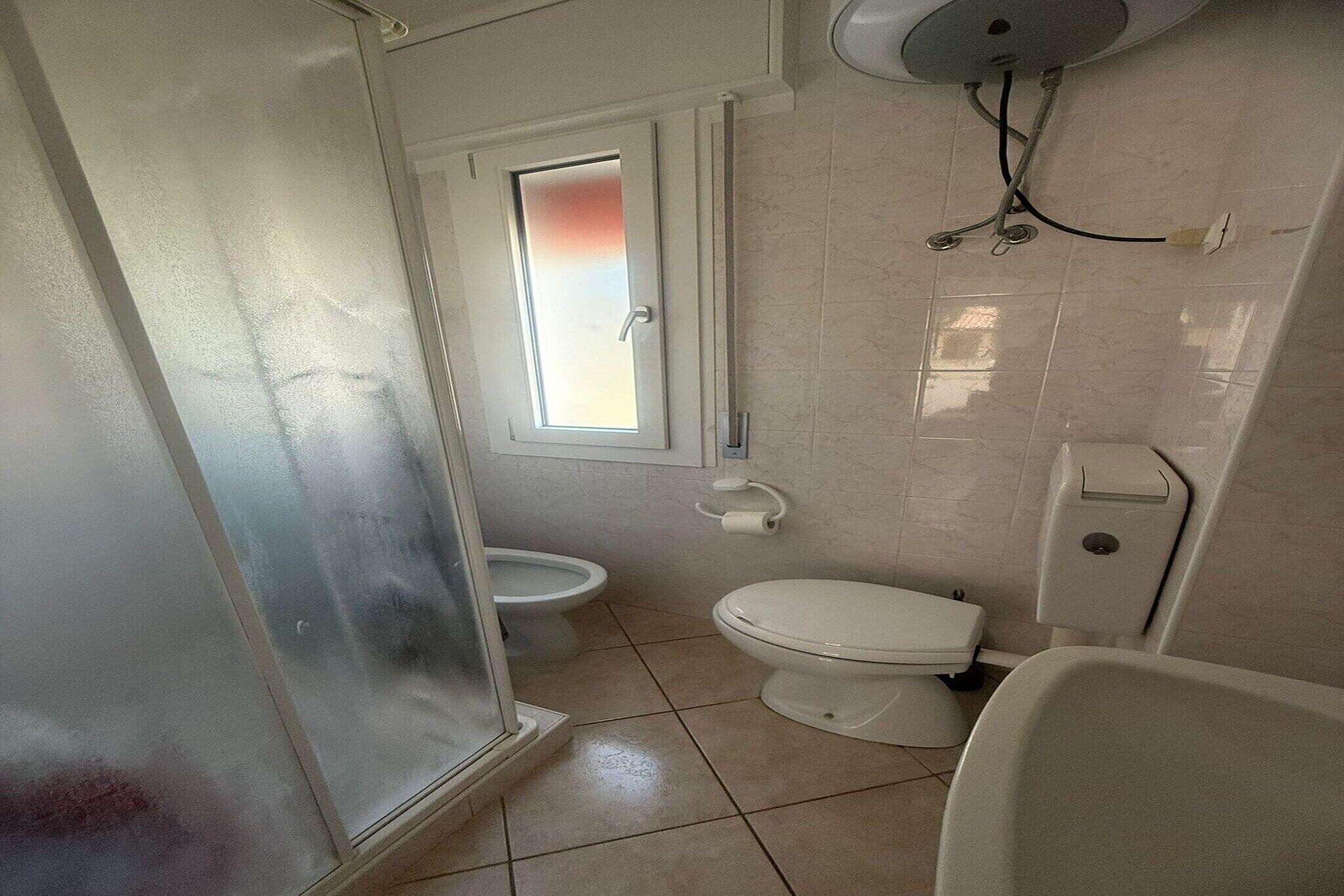 A small bathroom with a toilet, bidet, and a window.