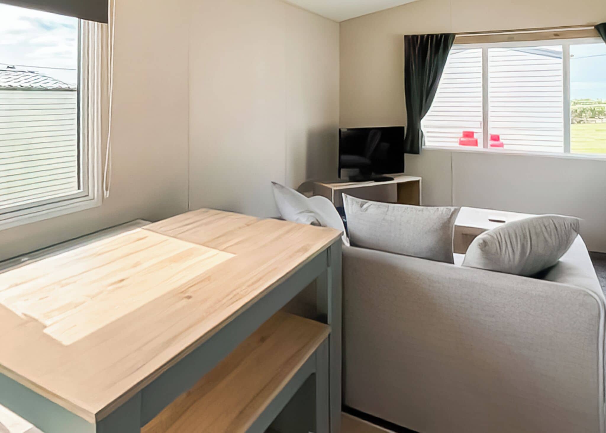 A compact room with a bunk bed, a sofa, a television, and a window with blinds.