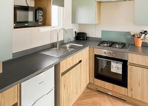 A modern kitchen with a stainless steel sink, a gas stove, and wooden cabinets. - 2 bedroom accommodation in Haverigg, Millom (Haverigg, Millom)