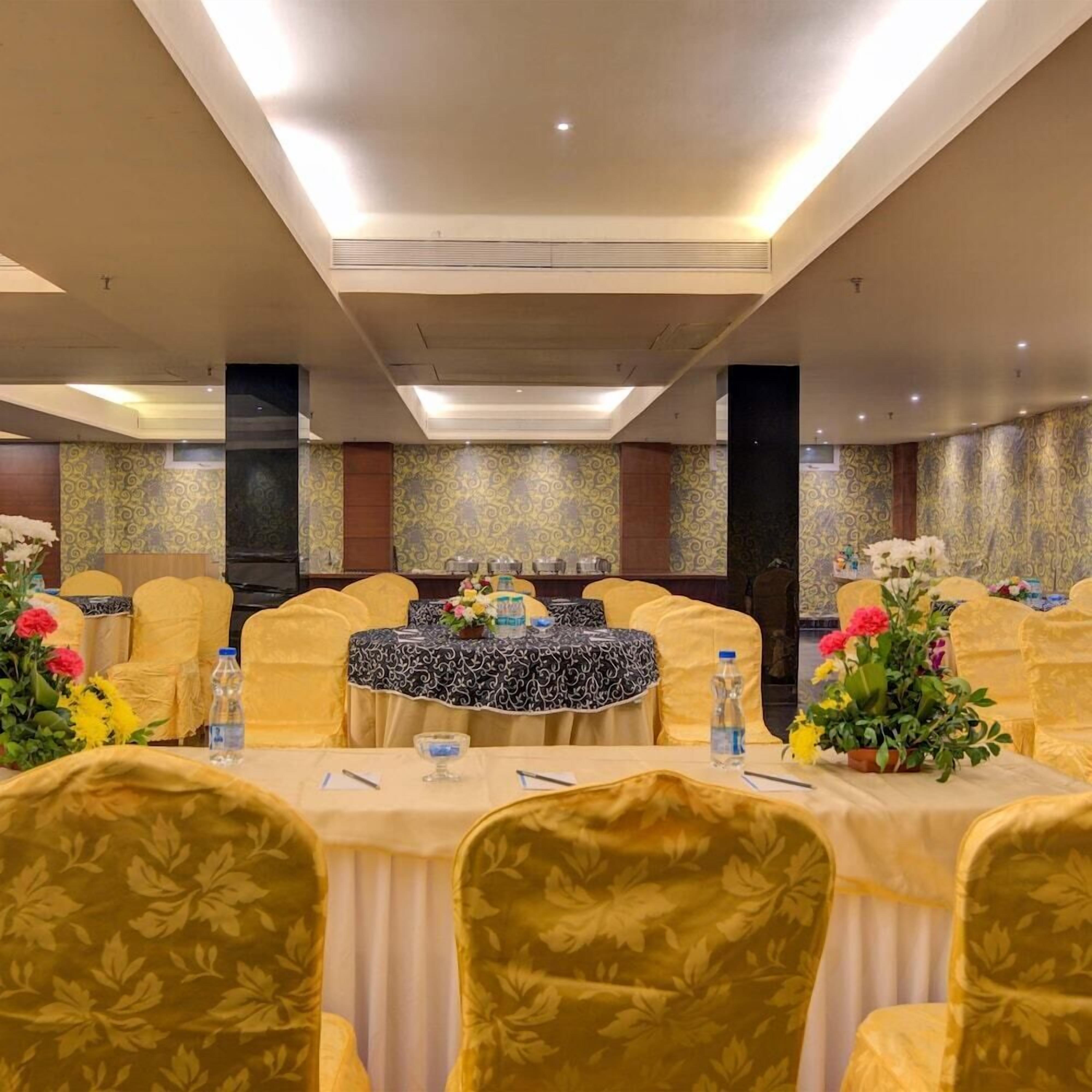 Un salón de conferencias con mesas redondas, sillas amarillas y centros de mesa florales.