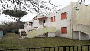 Ein Gebäude mit einer Treppe, die zu einem überdachten Eingang führt, umgeben von einer Rasenfläche und einem Baum.