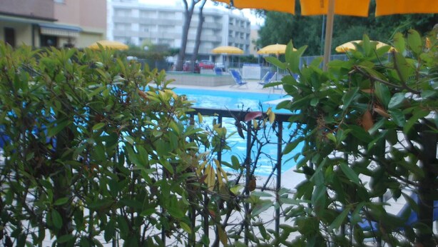 A pool area with yellow umbrellas, surrounded by greenery and buildings in the background. - Holiday Apartment in Rosolina Mare (Rosolina Mare)