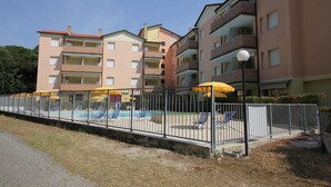 A multi-story residential building with balconies, a swimming pool, and a fenced outdoor area with sun loungers. - Holiday Apartment in Rosolina Mare (Rosolina Mare)