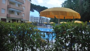 A pool area with yellow umbrellas, a building with balconies, and greenery in the foreground. - Holiday Apartment in Rosolina Mare (Rosolina Mare)