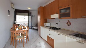 A kitchen with wooden cabinets, a white countertop, and a dining area with a table and chairs. - Holiday Apartment in Rosolina Mare (Rosolina Mare)