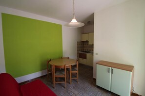 A compact kitchen with a dining area, a red sofa, and a green wall.