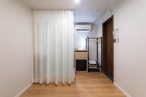 A hallway with a wooden floor, a curtained window, a small kitchenette, and a door with a shoe rack. - K Pop Residence I (Seoul)