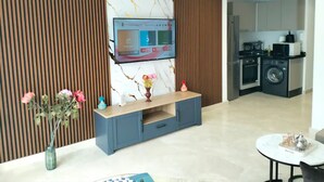 Una sala de estar moderna con un televisor de pantalla plana montado en una pared de mármol, un mueble de entretenimiento azul y una pequeña mesa con objetos decorativos.