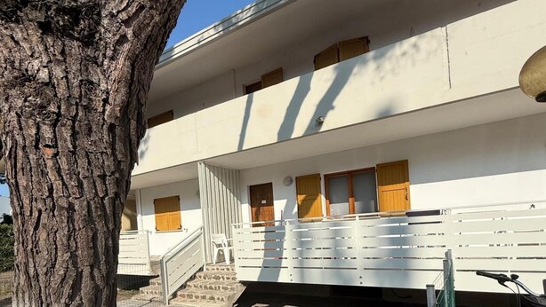 Ein zweigeschossiges Gebäude mit weißer Fassade, Holztüren und einer Treppe, die zum Eingang führt.