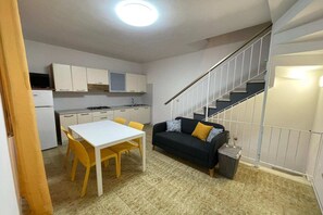 Een ruimtelijk ingerichte leefruimte met een kitchenette, een eethoek en een trap.