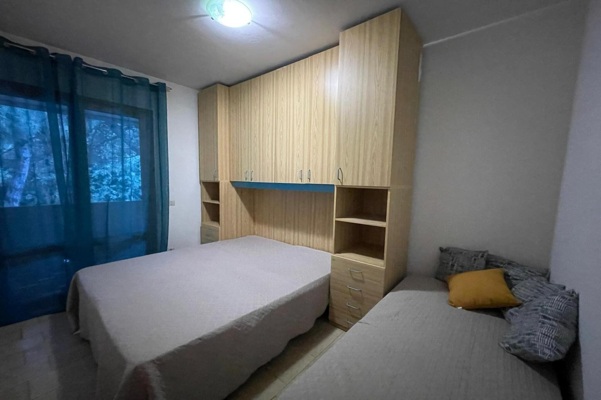 A bedroom with two beds, a wardrobe, and a window with curtains.