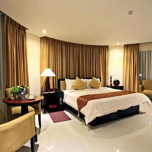 A hotel room with a bed, a bedside table, a lamp, a chair, and a small table with a vase and a water bottle. - Hotel Centro Puerto Princesa Near Airport by Zuzu (Puerto Princesa)