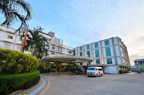 A hotel entrance with a curved canopy, palm trees, and a white van parked in front. - Hotel Centro Puerto Princesa Near Airport by Zuzu (Puerto Princesa)