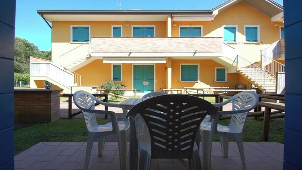 A two-story building with a yellow facade, a green door, and multiple windows. There is a patio area with outdoor furniture. - Apartment for Six in Rosolina (Rosolina Mare RO)