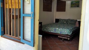 Ein Zimmer mit einem Bett, einem Fenster mit Holzrahmen und einem Fliesenboden.