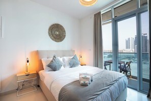 A hotel room with a bed, two bedside lamps, a decorative wall piece, and a view of a cityscape through large windows. - Bloomfields Studio in Julphar-Al Reem (Abu Dhabi)
