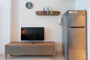 A modern kitchen with a built-in refrigerator, a flat-screen TV on a wooden cabinet, and a wall-mounted clock.