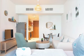 A modern hotel room with a bed, a sofa, a dining table with chairs, a TV, a washing machine, and a kitchen area. - Bloomfields Studio in Julphar-Al Reem (Abu Dhabi)