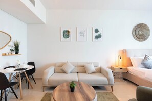 A modern living room with a sofa, a dining table, and a coffee table. There are wall art pieces and a decorative wall hanging.