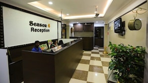 Zona de recepció amb terra de pissos, un taulell de recepció, un rellotge i una pantalla de televisió.