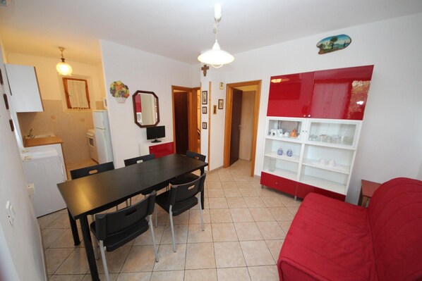 A compact living space with a dining area, kitchenette, and a red sofa.