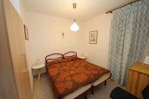 A bedroom with a bed, bedside tables, a desk, a chair, a cross on the wall, and a curtain.