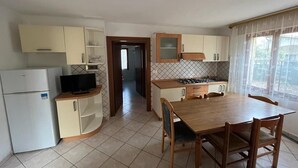 A compact kitchen with a dining area, a refrigerator, a stove, and a television. - Solaris, trilocale: 72  (Rosolina Mare RO)