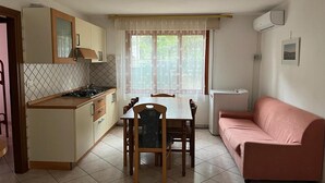 A compact kitchen with a dining table and chairs, a pink sofa, and a window with sheer curtains. - Solaris, trilocale: 72  (Rosolina Mare RO)