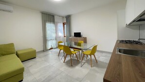 A modern kitchen with a dining area, a sofa, and a TV. - Cozy Apartment in Rosolina for 4 (Rosolina Mare RO)