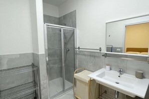 A modern bathroom with a glass-enclosed shower, a white sink with a mirror above, and a towel rack. - Cozy Apartment in Rosolina for 4 (Rosolina Mare RO)