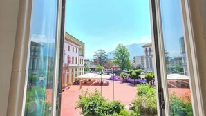 Vista a través de una ventana que muestra un patio con edificios, una zona cubierta y vegetación.