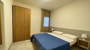 Ein Schlafzimmer mit Bett, Nachttisch, Holzschrank und einem fenster mit Vorhängen.