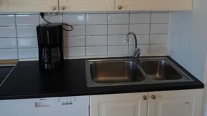 Ett kök med vita skåp, en svart bänkskiva, en diskho i rostfritt stål och en kaffebryggare.