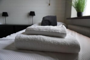 A neatly made bed with two folded white towels and a grey pillow. - Vannebodagatan (Frövi)