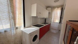 Une cuisine de taille réduite, équipée d’un lave-linge, d’un évier et de meubles de rangement rouges.