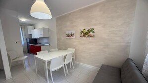Une cuisine moderne avec des meubles blancs, une table à manger avec des chaises et un canapé gris.