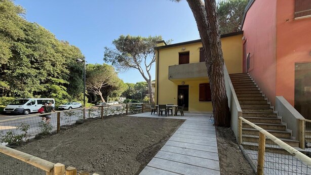 Un edificio con una scala che conduce a un balcone, un vialetto lastricato e un'area giardino recintata.