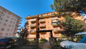 Un edificio residenziale a più piani con balconi, un ingresso chiuso da cancello e auto parcheggiate.