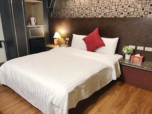 A hotel room with a large bed, a nightstand with a lamp, a telephone, and a small table with a vase of flowers. - Fuchang Hotel (Taipei)