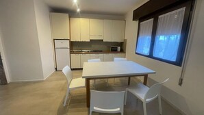 Una cocina compacta con armarios blancos, microondas y un comedor con mesa y sillas blancas.