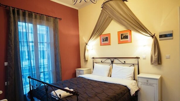 A bedroom with a bed, curtains, a nightstand, and a wall with framed pictures. - Acronafplia Pension B&D (Nafplio)