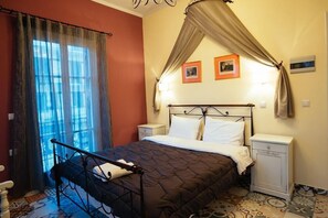 A bedroom with a bed, curtains, a nightstand, and a wall with framed pictures. - Acronafplia Pension B&D (Nafplio)